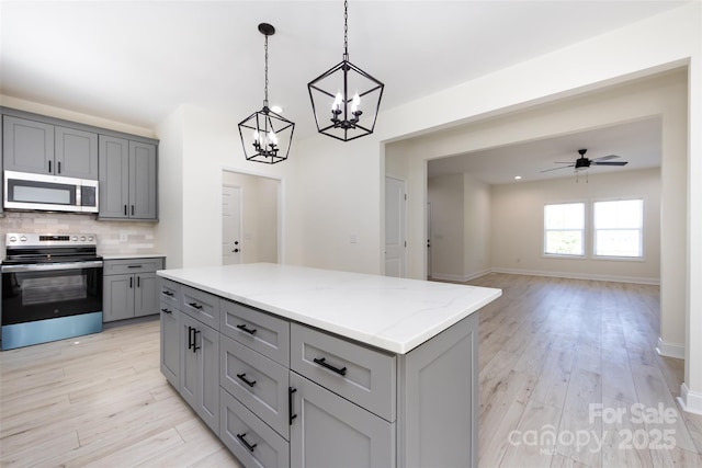 kitchen featuring light stone countertops, gray cabinetry, light wood finished floors, stainless steel appliances, and tasteful backsplash
