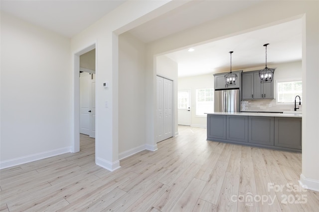 kitchen with freestanding refrigerator, a notable chandelier, light wood finished floors, and gray cabinetry