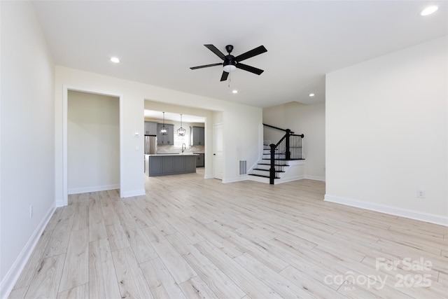 unfurnished living room featuring light wood finished floors, stairway, a ceiling fan, and visible vents