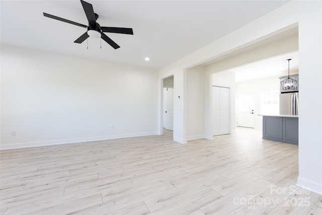unfurnished living room featuring ceiling fan with notable chandelier, light wood-type flooring, baseboards, and recessed lighting