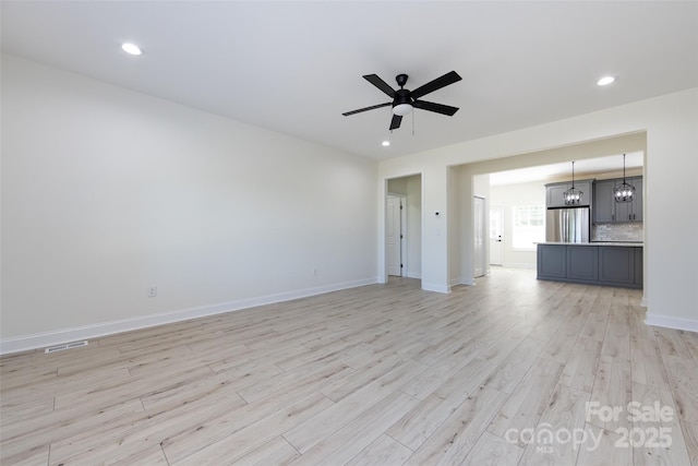 unfurnished living room featuring light wood finished floors, ceiling fan with notable chandelier, visible vents, baseboards, and recessed lighting