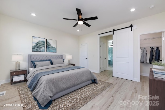 bedroom featuring a closet, light wood-style flooring, a barn door, baseboards, and a spacious closet