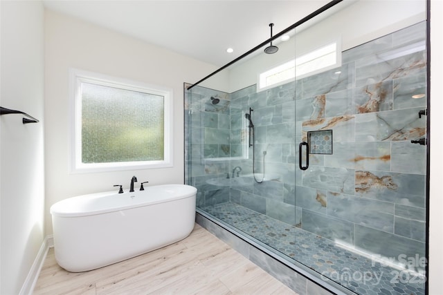 full bathroom featuring a stall shower, baseboards, a freestanding bath, and wood finished floors