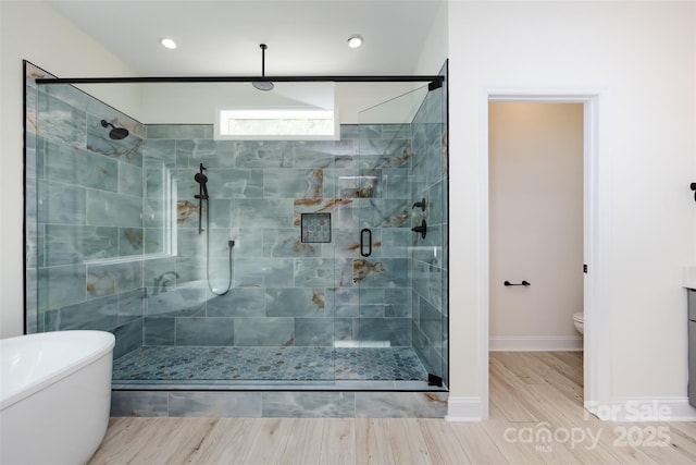 bathroom with toilet, wood finished floors, a freestanding bath, baseboards, and a shower stall