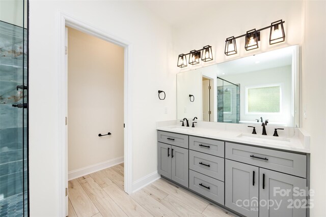 full bathroom featuring a stall shower, baseboards, double vanity, and a sink