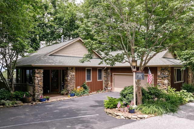view of front of house with roof with shingles, stone siding, a garage, and aphalt driveway