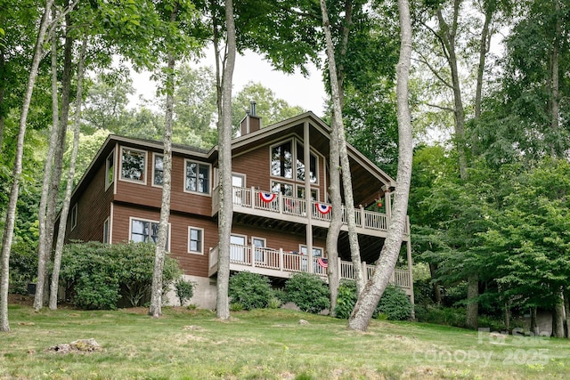 back of house with a chimney, a balcony, and a yard
