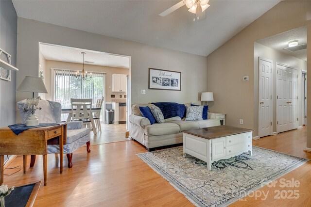 living area featuring ceiling fan with notable chandelier, vaulted ceiling, and light wood-type flooring