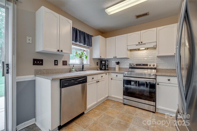 kitchen with under cabinet range hood, visible vents, a sink, decorative backsplash, and appliances with stainless steel finishes