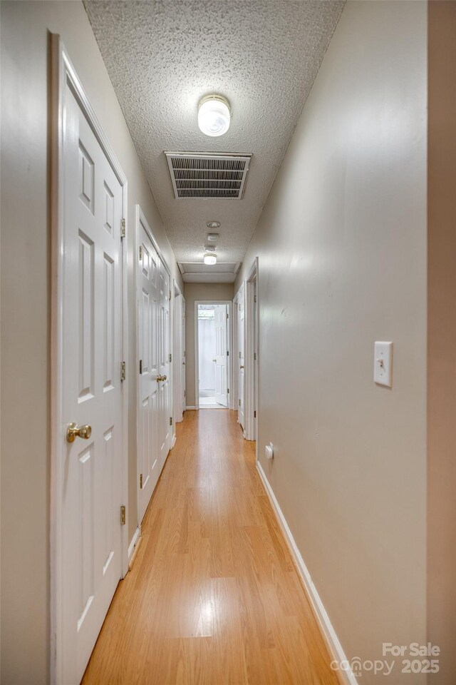 hall with baseboards, light wood-style floors, visible vents, and a textured ceiling