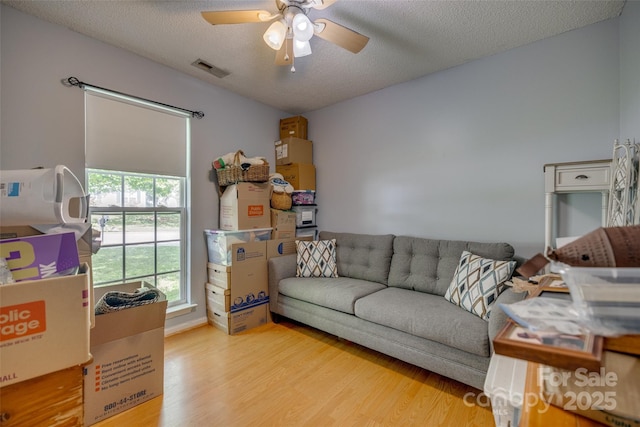 living area featuring visible vents, wood finished floors, a textured ceiling, and ceiling fan