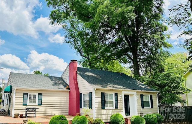 view of front of property with a chimney, a shingled roof, fence, and a patio area