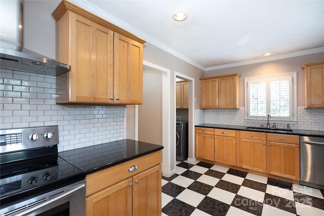 kitchen featuring stainless steel appliances, wall chimney exhaust hood, a sink, dark countertops, and washer / clothes dryer
