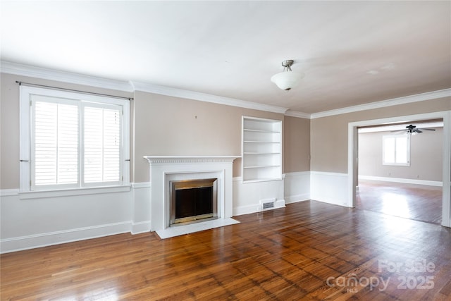 unfurnished living room featuring built in features, a fireplace with flush hearth, a ceiling fan, baseboards, and wood finished floors