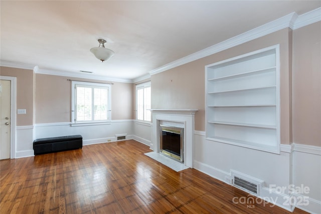 unfurnished living room featuring wood finished floors, built in features, a fireplace, and ornamental molding