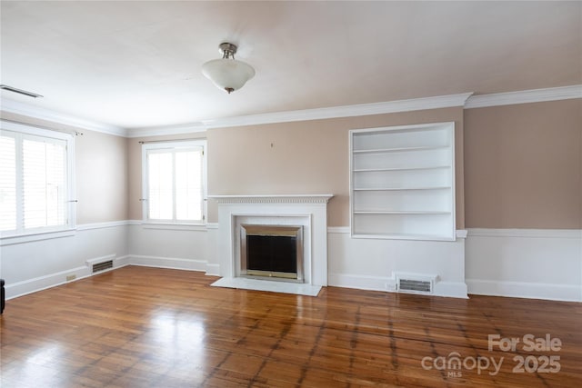 unfurnished living room featuring built in shelves, a fireplace with flush hearth, wood finished floors, ornamental molding, and baseboards