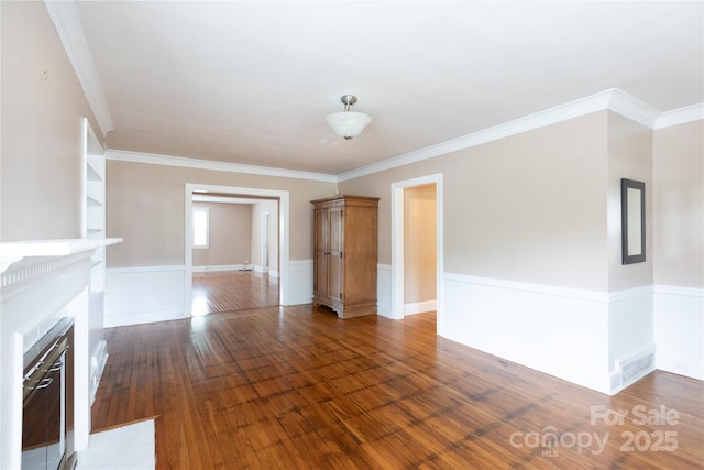 unfurnished living room featuring a fireplace with flush hearth, crown molding, wood finished floors, and a wainscoted wall