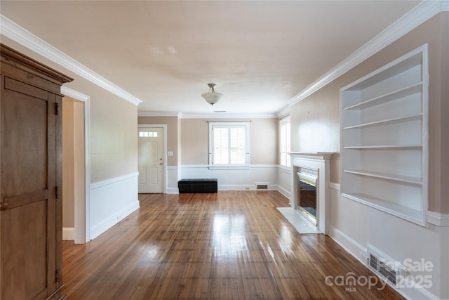 unfurnished living room featuring wood-type flooring, a premium fireplace, built in shelves, ornamental molding, and a wainscoted wall