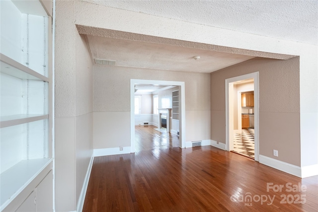 unfurnished room with wood finished floors, baseboards, a textured ceiling, and a smoke detector