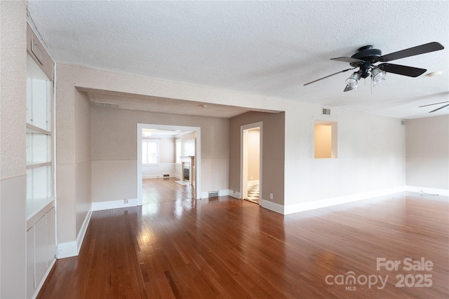 unfurnished living room with wood finished floors, a ceiling fan, a textured ceiling, and baseboards