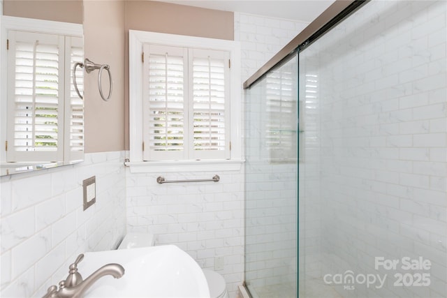 full bathroom with a stall shower, tile walls, a sink, and a wainscoted wall