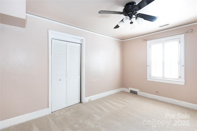 unfurnished bedroom with ornamental molding, carpet, a closet, baseboards, and ceiling fan