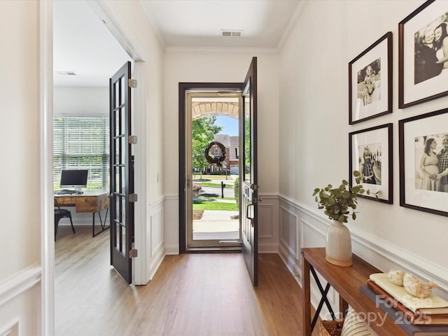 entryway featuring visible vents, ornamental molding, a wainscoted wall, and light wood-type flooring