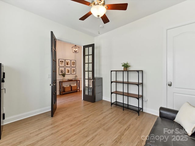 living area with baseboards, ceiling fan with notable chandelier, and light wood-type flooring