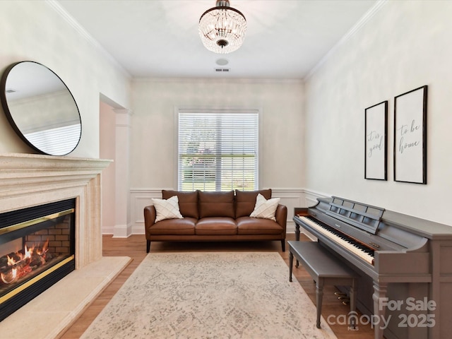 living area with crown molding, a fireplace, a wainscoted wall, wood finished floors, and visible vents