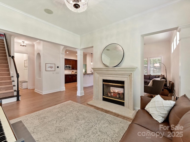 living area featuring stairs, arched walkways, crown molding, and light wood-type flooring