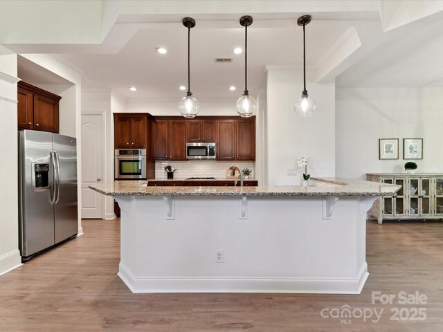 kitchen with light wood-type flooring, tasteful backsplash, a kitchen bar, and stainless steel appliances