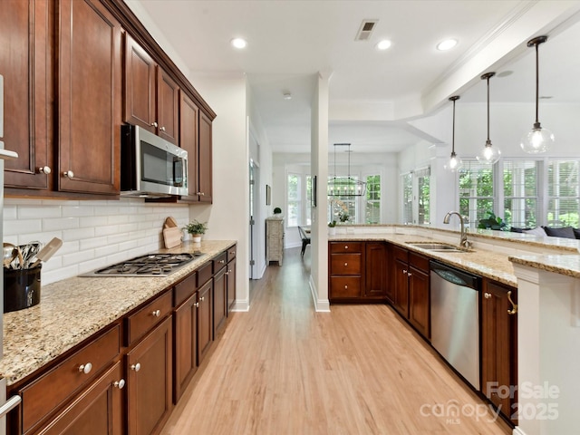 kitchen featuring decorative light fixtures, tasteful backsplash, a sink, light wood finished floors, and stainless steel appliances