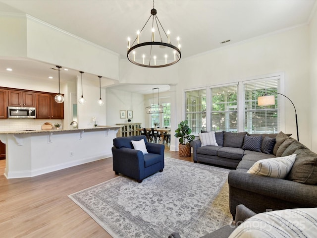 living area with an inviting chandelier, crown molding, light wood-style flooring, and visible vents