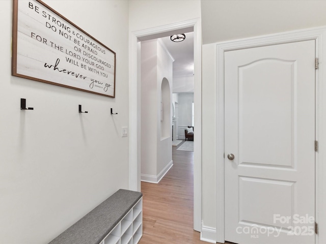 mudroom featuring arched walkways, baseboards, and light wood-style flooring