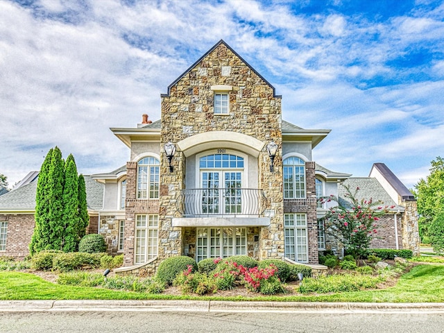 view of front of property with a chimney, stucco siding, a balcony, and stone siding