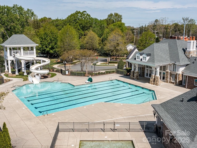 community pool featuring a patio, a water slide, and fence