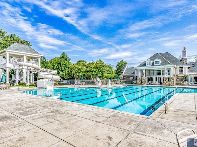 community pool with fence, a water slide, and a patio