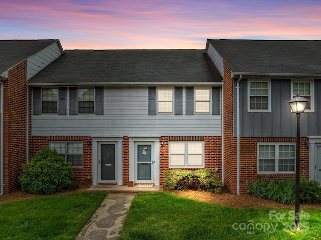 multi unit property with board and batten siding, a front lawn, and brick siding