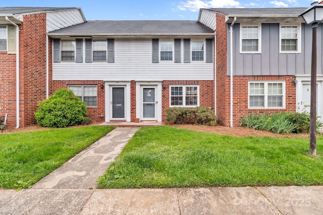 townhome / multi-family property with board and batten siding, a front yard, and brick siding