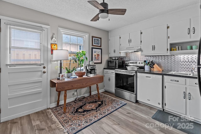 kitchen featuring ceiling fan, dark countertops, appliances with stainless steel finishes, under cabinet range hood, and light wood-style flooring