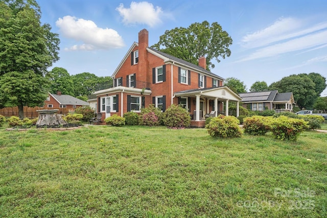 back of house with a lawn, a chimney, covered porch, and brick siding