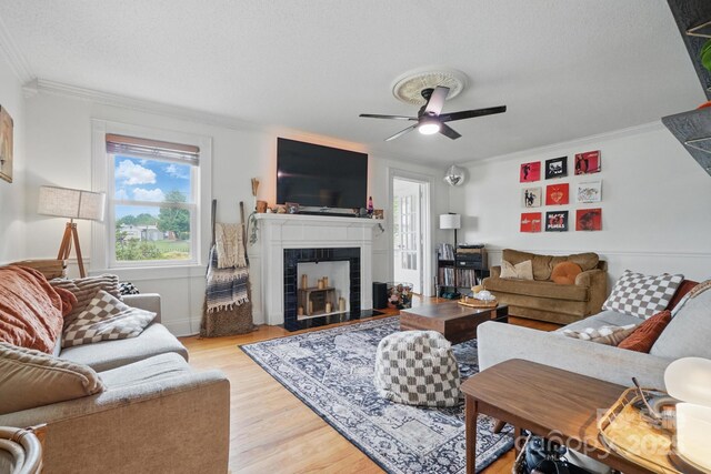 living area with a fireplace with flush hearth, ceiling fan, crown molding, and light wood-style flooring