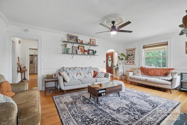 living area with a ceiling fan, arched walkways, crown molding, and light wood-type flooring