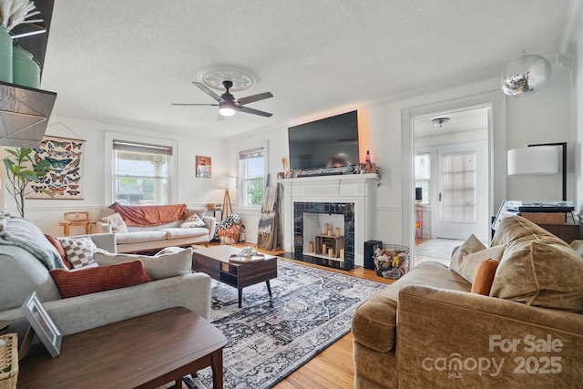 living area with a textured ceiling, wood finished floors, a tiled fireplace, and ceiling fan