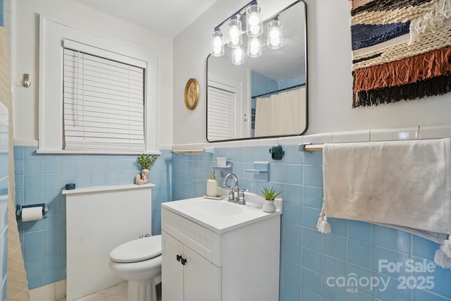 bathroom with tile patterned flooring, a wainscoted wall, toilet, vanity, and tile walls