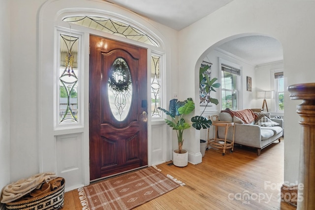 foyer featuring wood finished floors, arched walkways, and crown molding