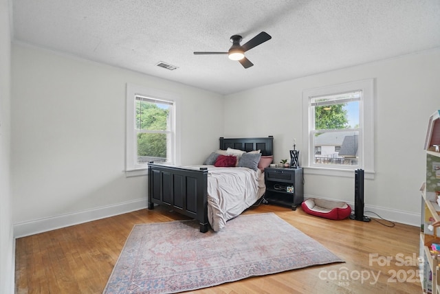 bedroom with wood finished floors, multiple windows, visible vents, and a textured ceiling
