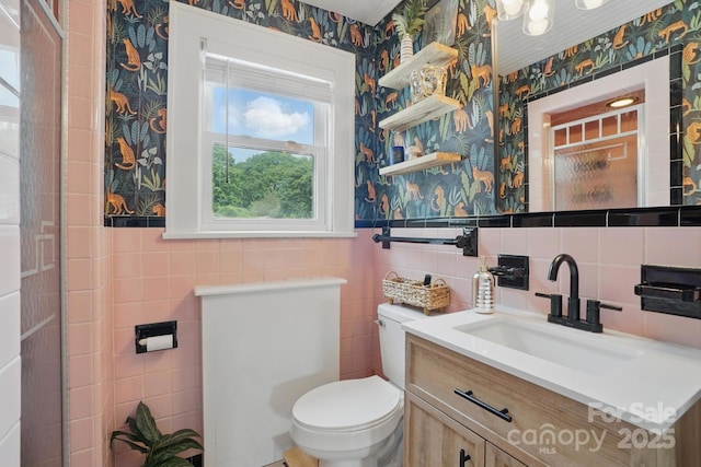 bathroom featuring wallpapered walls, wainscoting, vanity, tile walls, and toilet