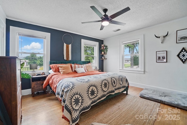bedroom featuring wood finished floors, visible vents, a textured ceiling, and ornamental molding