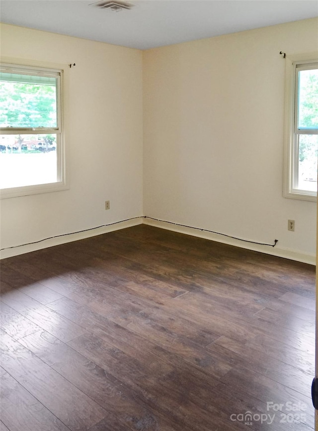 empty room with baseboards, dark wood-style flooring, and visible vents